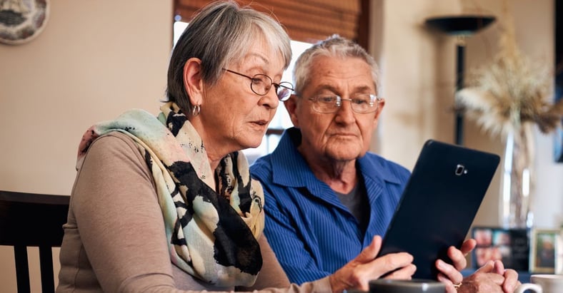 elderly man and woman holding a tablet at the table