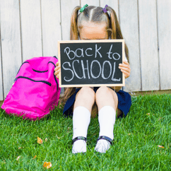 young child hiding behind back to school sign
