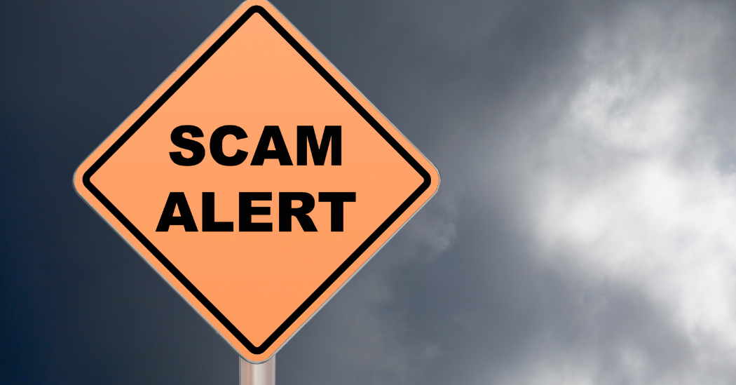 Bright orange road-style sign reading “Scam Alert” against a dark, cloudy sky, symbolizing a warning about potential fraud or scams.