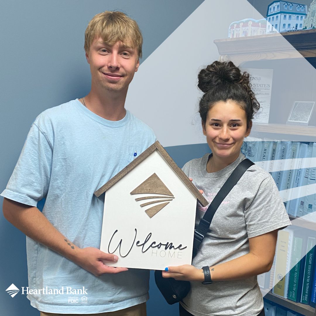 Young couple holding a 'Welcome Home' sign after closing on their first home with Heartland Bank in Grand Island, Nebraska.